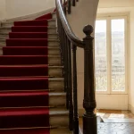 cage d'escalier immeuble rénové avec rampe bois et tapis rouge